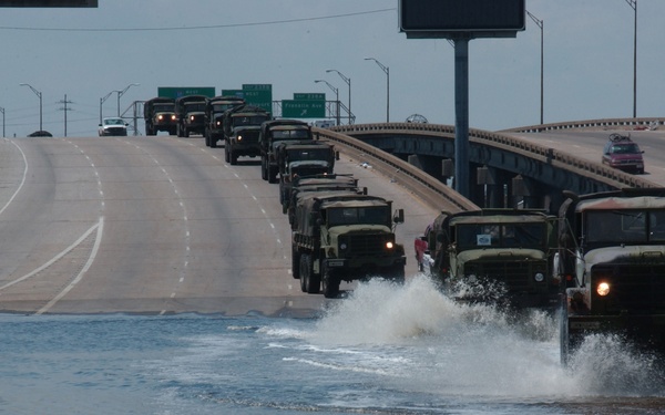 A convoy of military vehicles crosses floodwaters on Interstate 10.