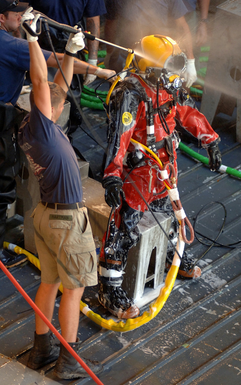 Navy divers use a power washer to clean and sanitize another diver.