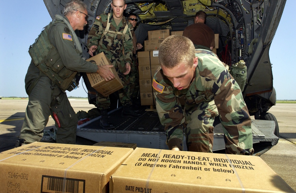 Military personnel load hundreds of meals, ready to eat and water onto a CH-47 Chinook helicopter.