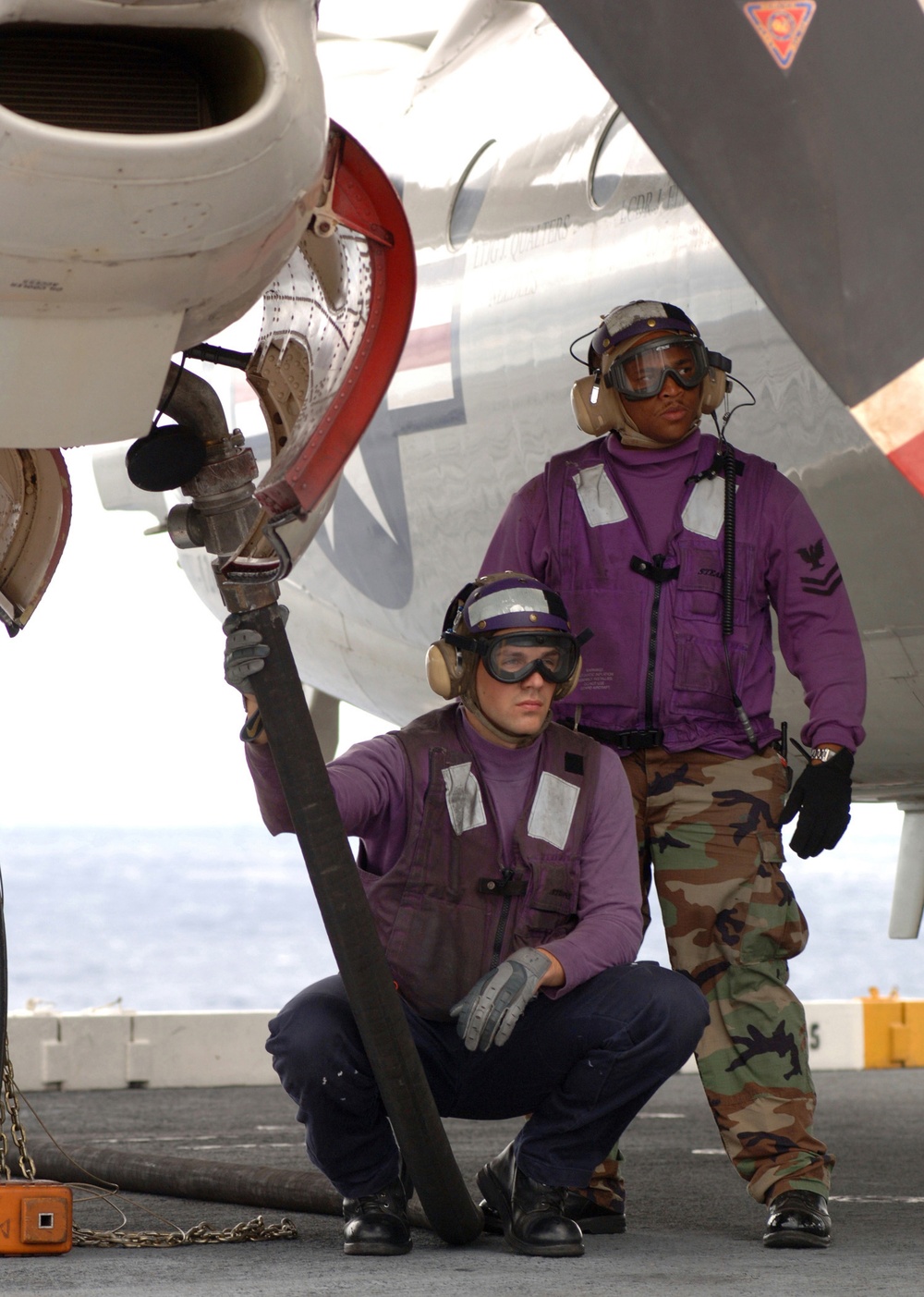 U.S. Navy sailors refuel an E-2C Hawkeye during flight operations.