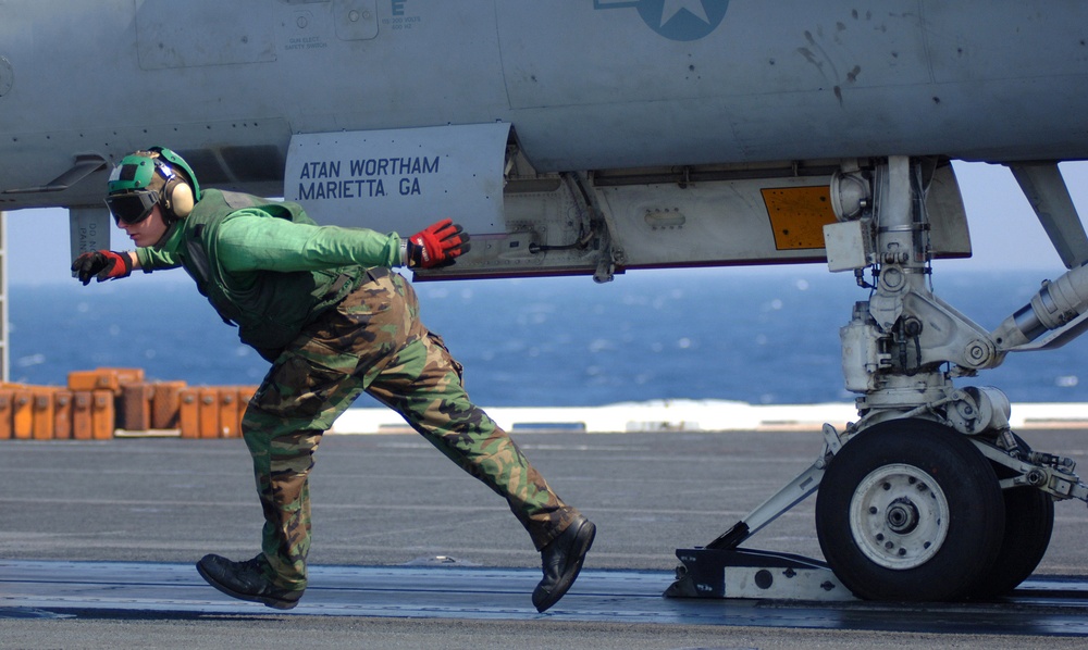 A Navy flight deck crewman runs from under an aircraft.