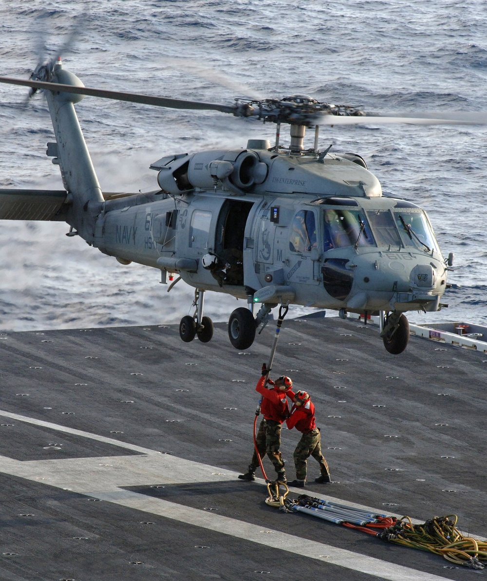 Sailors connect a set of replenishment slings to the cargo hook of an HH-60 Seahawk helicopter.