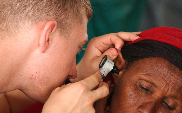 Corpsman Forrest Simmons uses an otoscope to inspect the ear of an elderly woman.