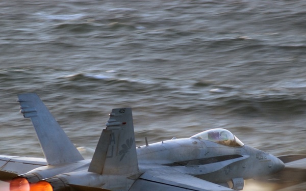 The afterburners of a Navy F/A-18 Hornet glow as the aircraft launches.