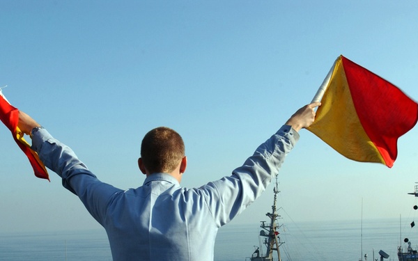 Navy Seaman Ryan Ruona uses semaphore flags to signal another ship.