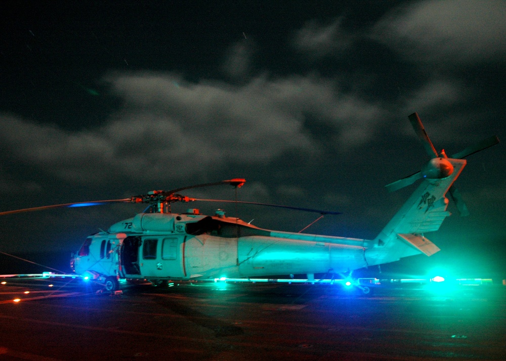 Flight deck lights illuminate a Navy SH-60 Seahawk helicopter.