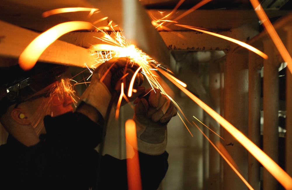 Sparks fly as U.S. Navy Fireman Derrick Young cuts through steel brackets.