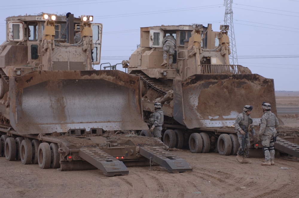 U.S. Army soldiers prepare to unload two armored Caterpillar D9 bulldozers.