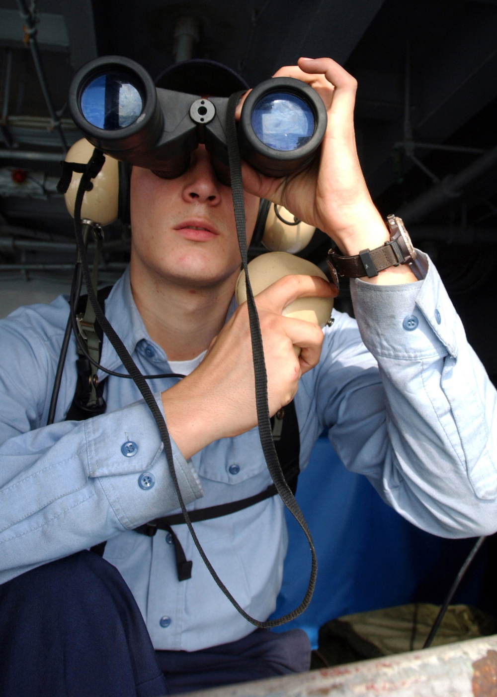 Navy Seaman Keith Ketterer uses his binoculars to search the horizon for any air or surface contacts.