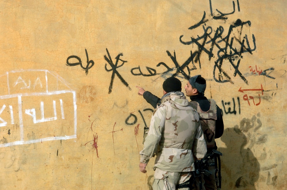 A U.S. Army soldier listens as an Iraqi interpreter explains the anti-American graffiti scrawled on a wall.