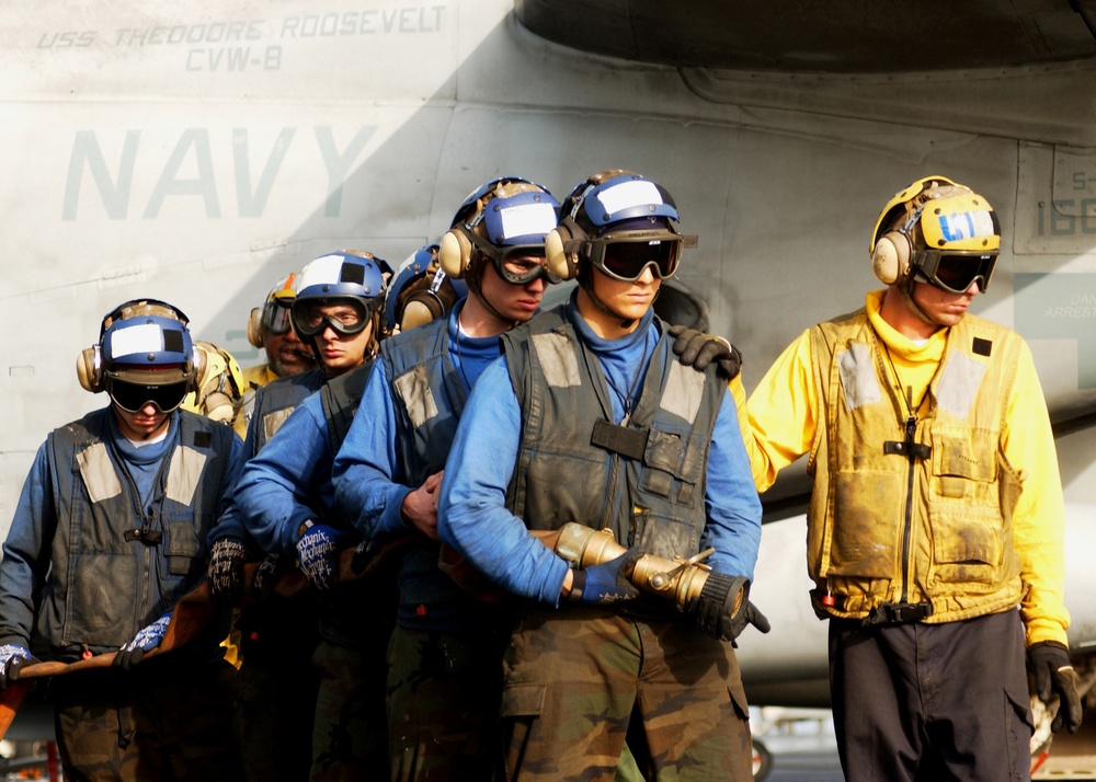 U.S. Navy flight deck personnel stand by with their fire hose.