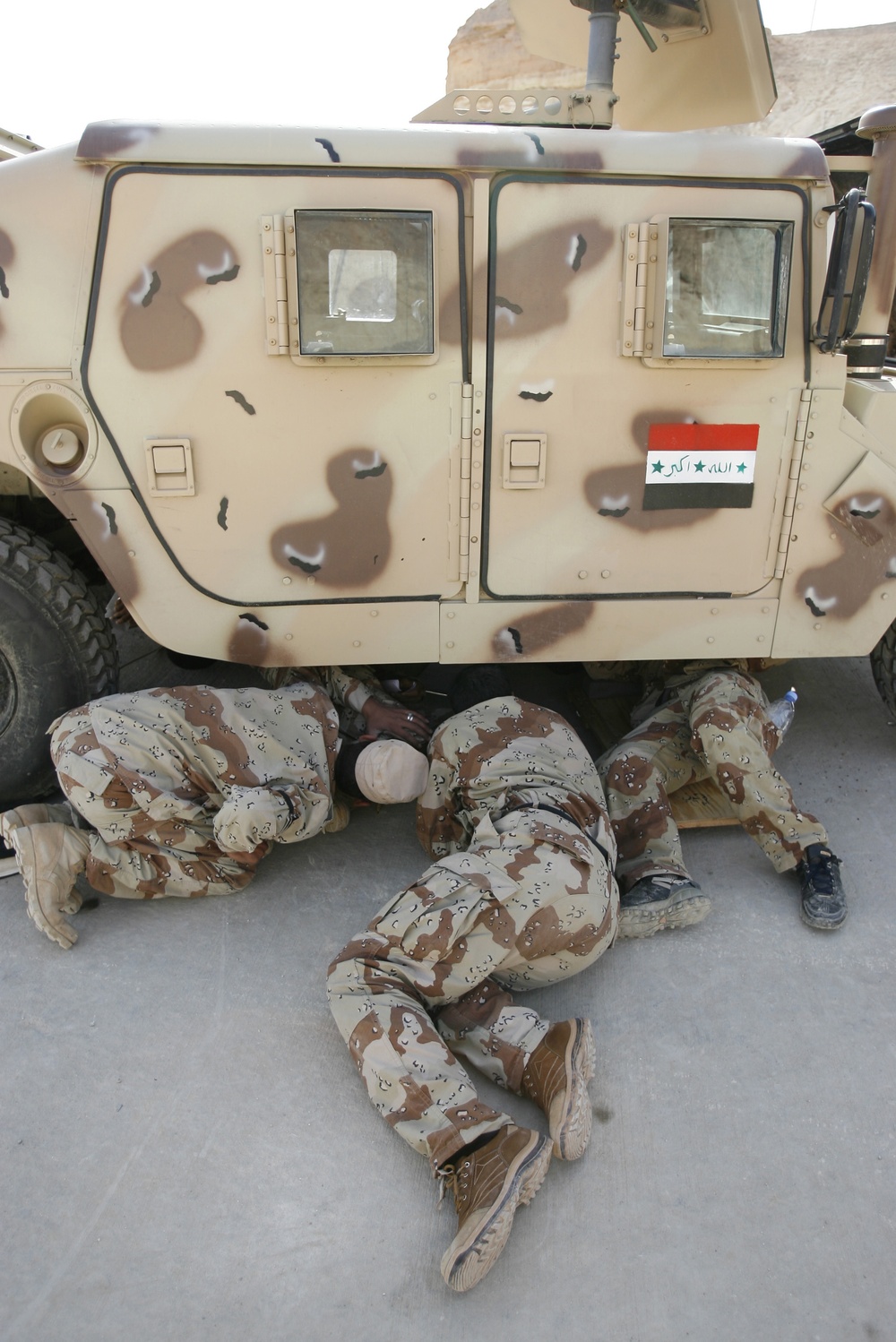 Iraqi army soldiers examine the underside of a Humvee.