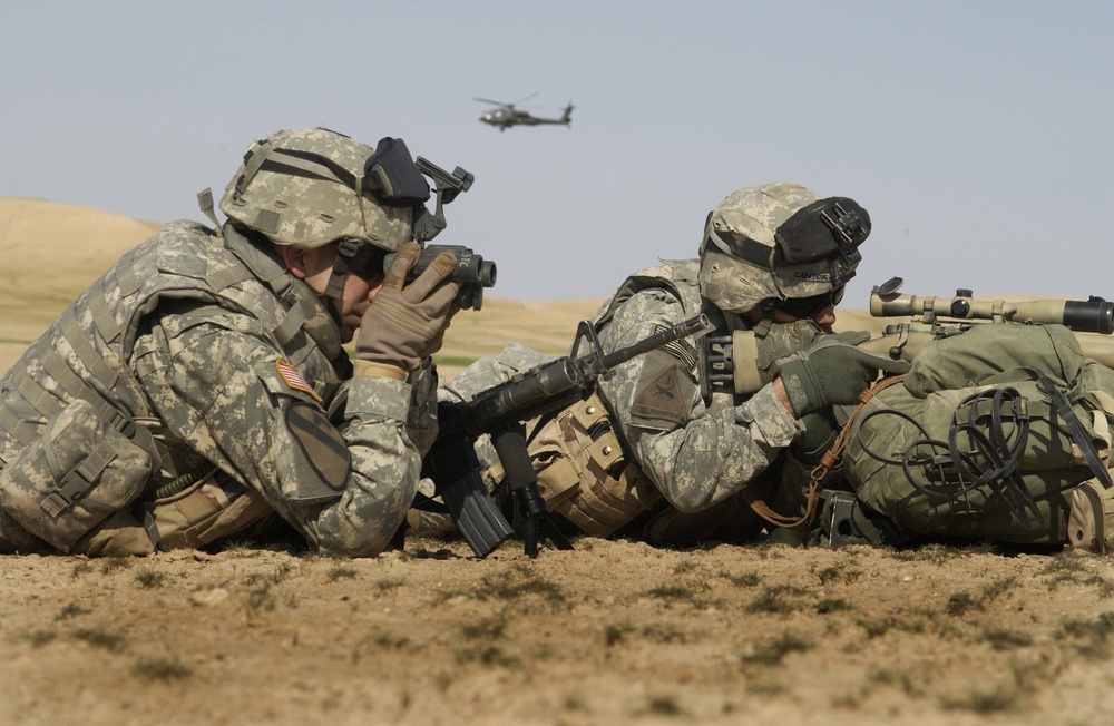 Two U.S. Army soldiers use binoculars and a riflescope to watch for insurgents.