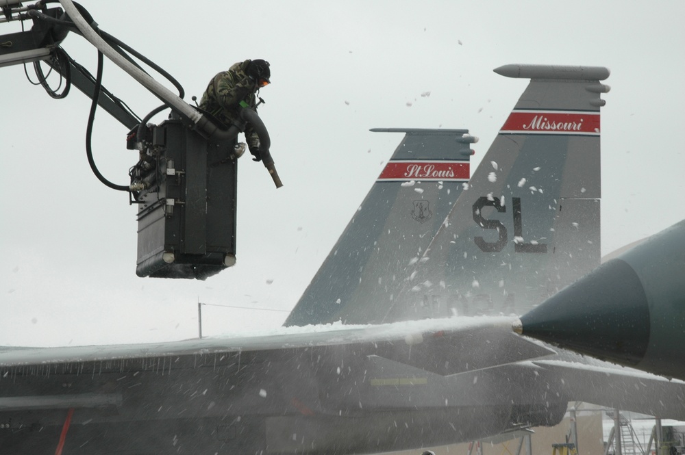 The snow flies as a U.S. Air Force airman de-ices an F-15C Eagle aircraft.