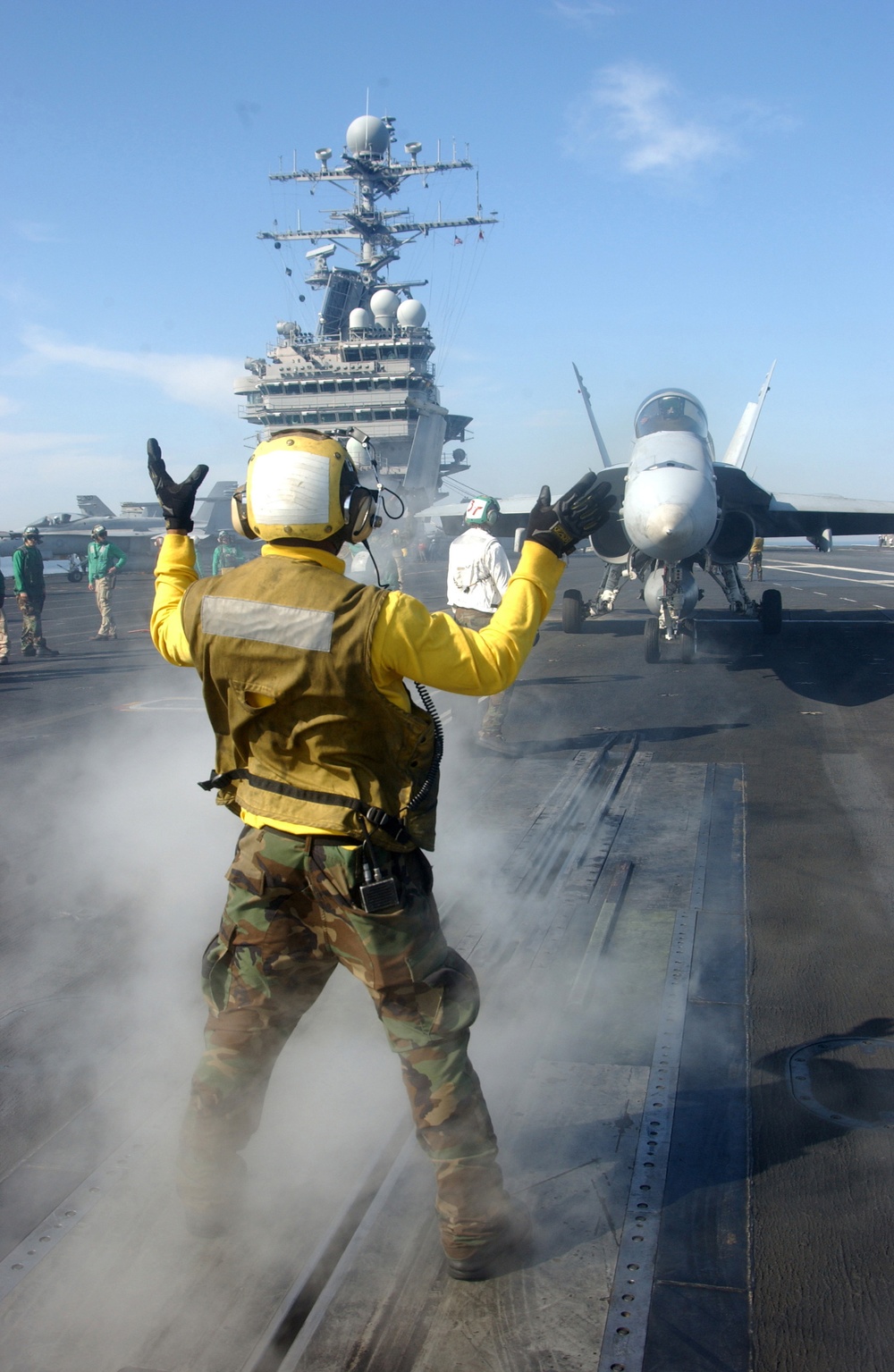A U.S. Navy plane handler guides an F/A-18C Hornet aircraft to a catapult.