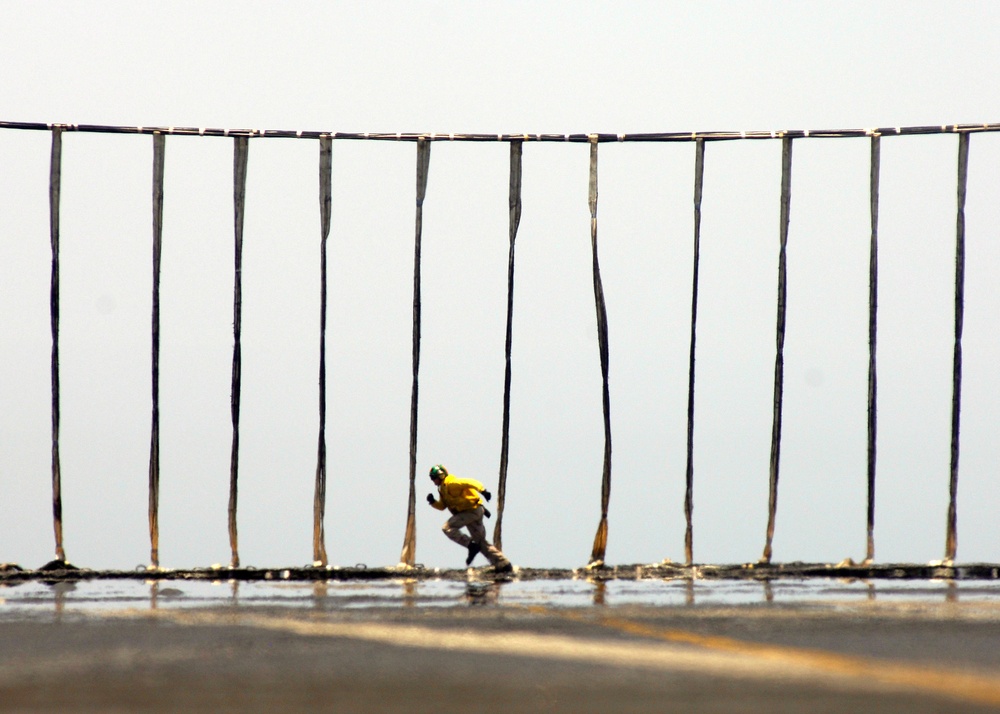 A flight deck officer runs along the length of an erected aircraft barricade.