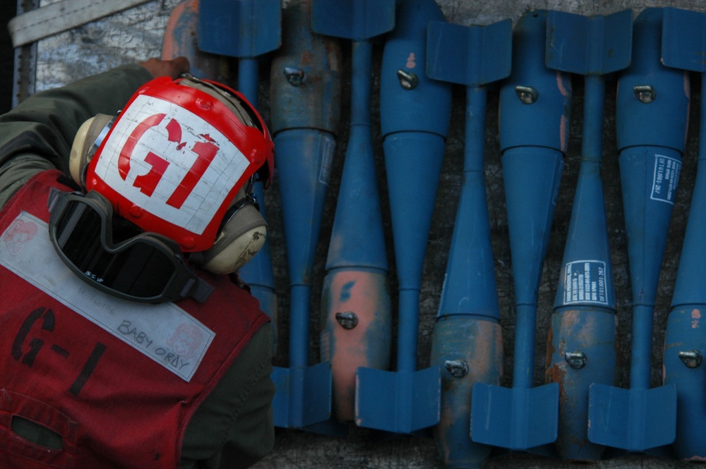 A U.S. Navy ordnanceman stacks blue MK-76 practice bombs.