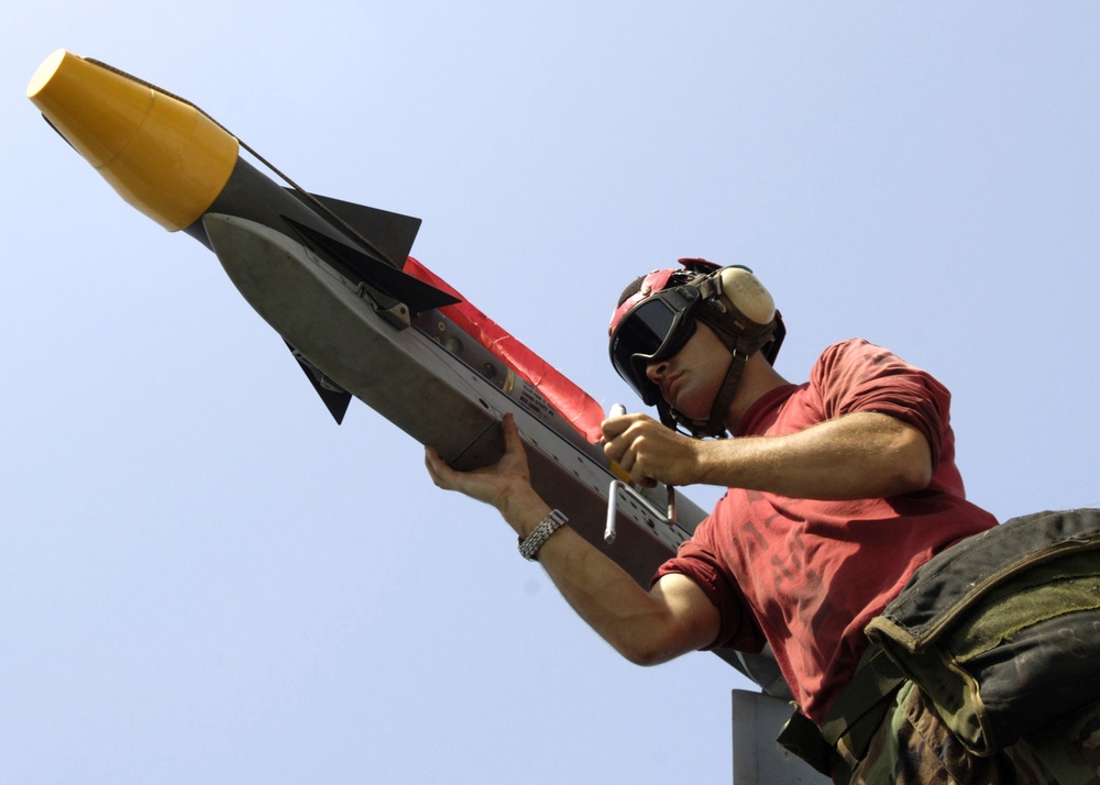 Petty Officer 3rd Class Nick Rowland attaches an AIM-9 Sidewinder missile.
