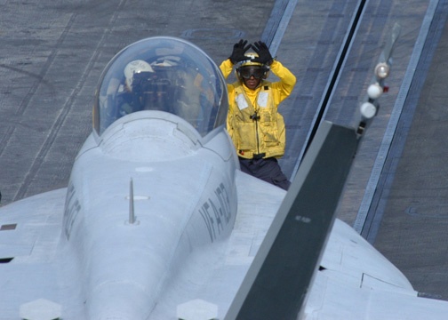 A Navy flight deck crewman uses hand signals to guide the pilot of an F/A-18 Hornet.