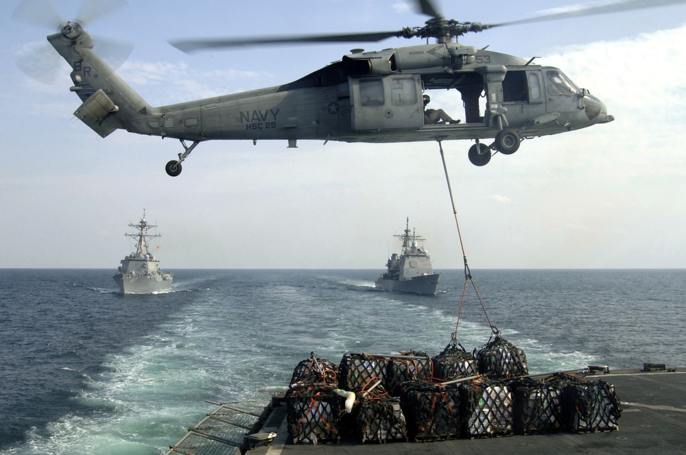 A MH-60S Nighthawk helicopter lifts cargo nets of supplies.