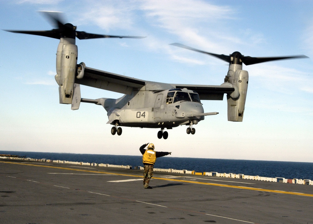 A flight deck crewman directs the crew of a U.S. Marine Corps CV-22 Osprey.