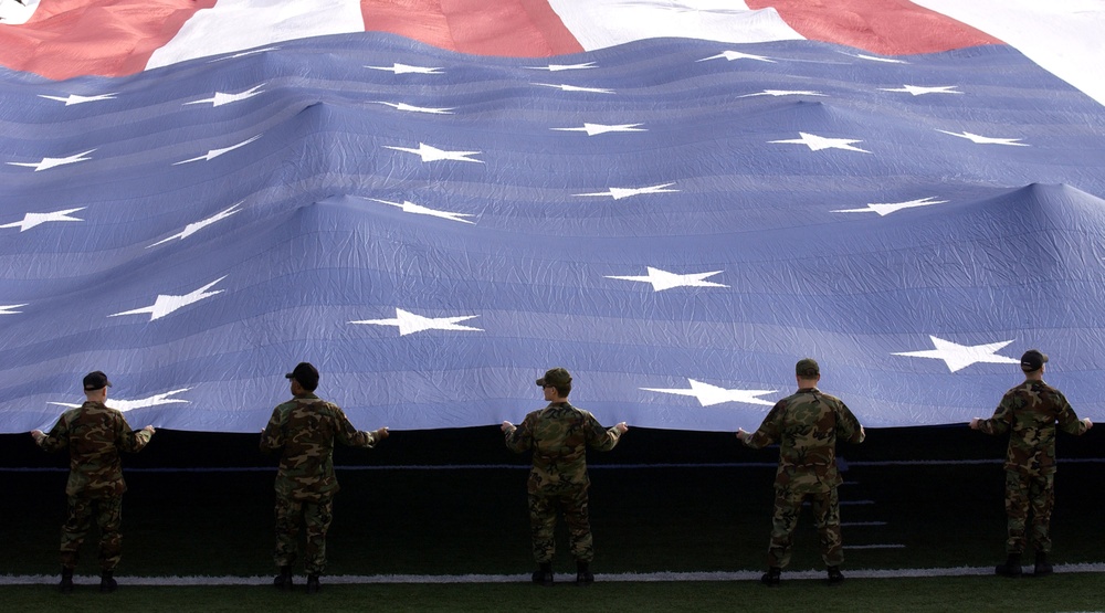 U.S. Air Force airmen grip the edge of a 100 X 50 yard American flag.