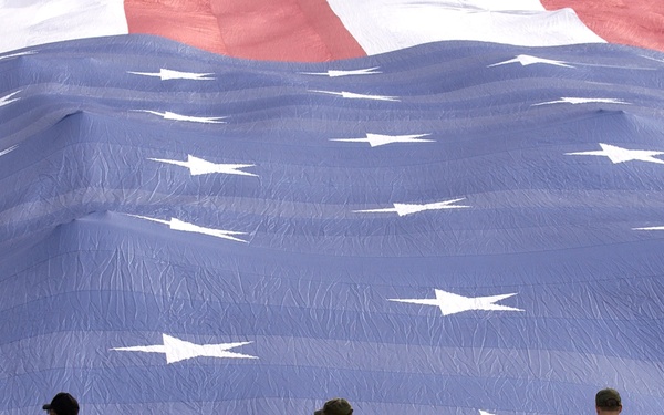 U.S. Air Force airmen grip the edge of a 100 X 50 yard American flag.