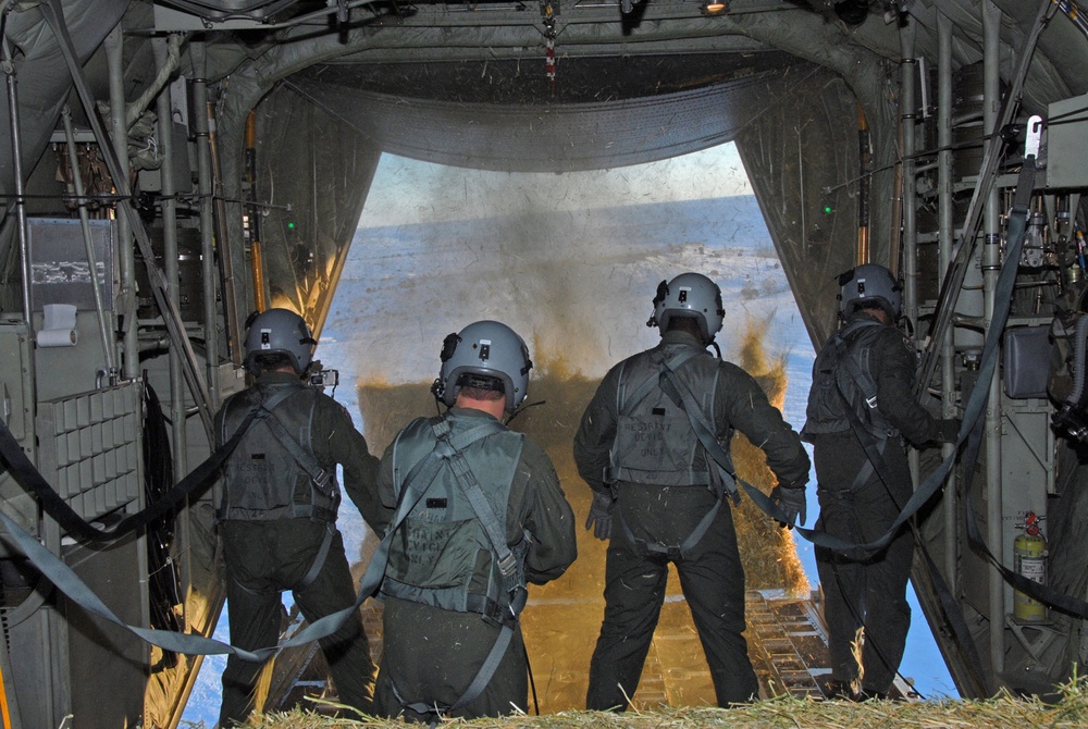 Wyoming Air National Guardsmen push bales of hay out of the back of a C-130 Hercules aircraft.