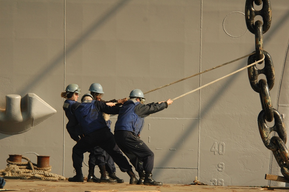 U.S. Navy sailors use a line to guide an anchor chain.