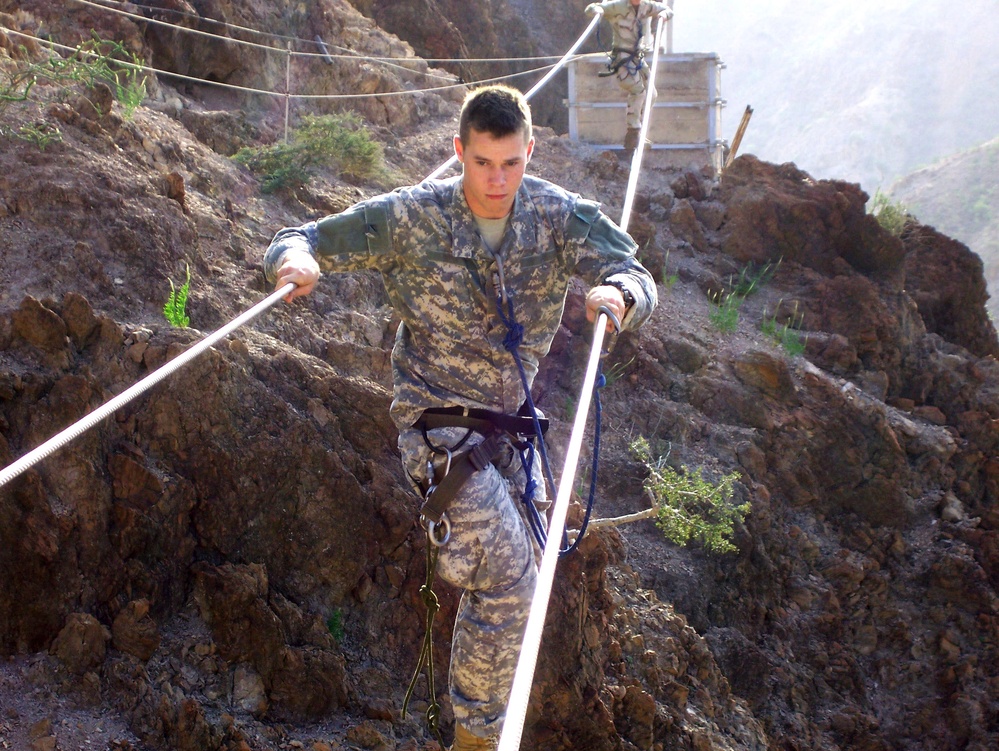 U.S. Army Spc. Anthony Slocomb crosses a three-rope bridge.