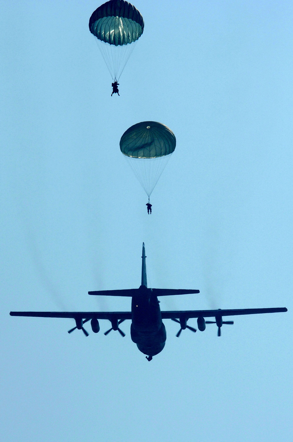 U.S. Air Force security forces airmen parachute from a C-130 Hercules aircraft.