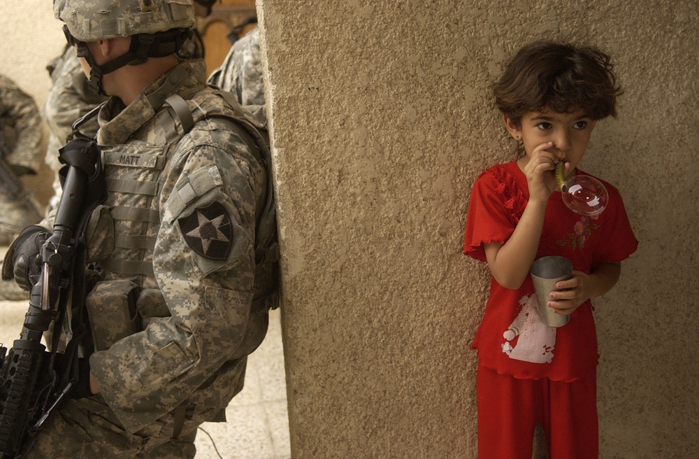An Iraqi girl blows bubbles while U.S. Army soldiers keep an eye on the street.