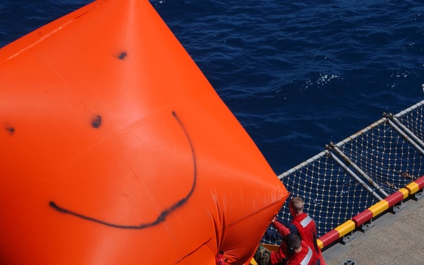 U.S. Navy sailors push an inflatable target overboard.