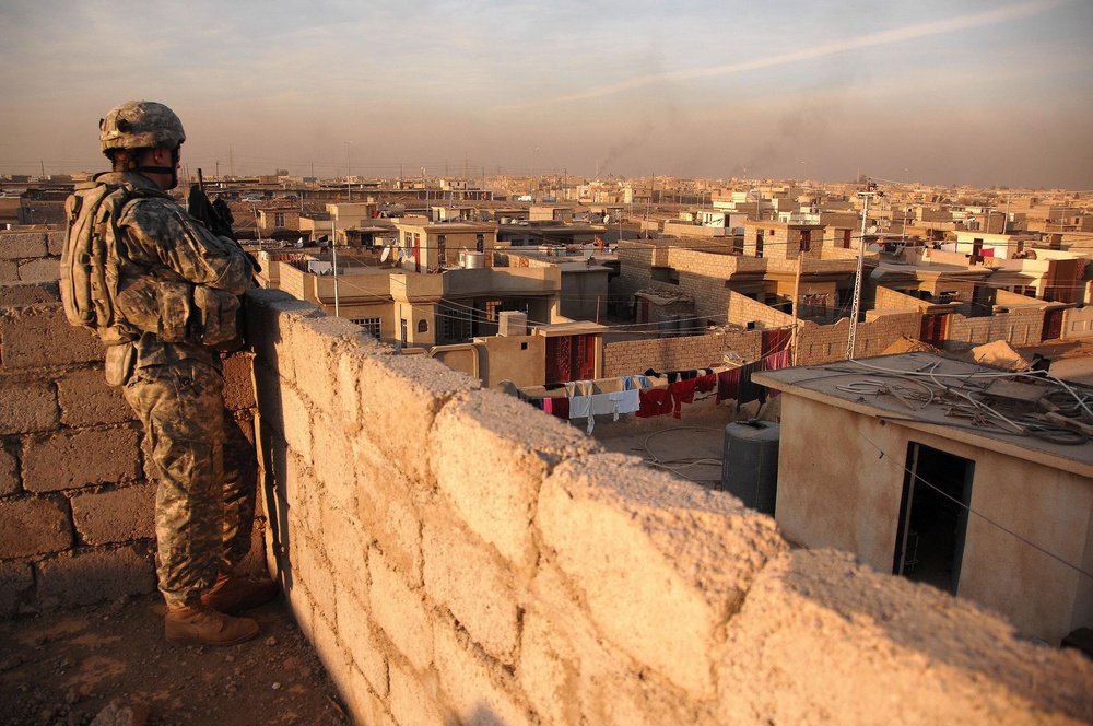 A U.S. Army soldier watches the neighborhood from a rooftop.