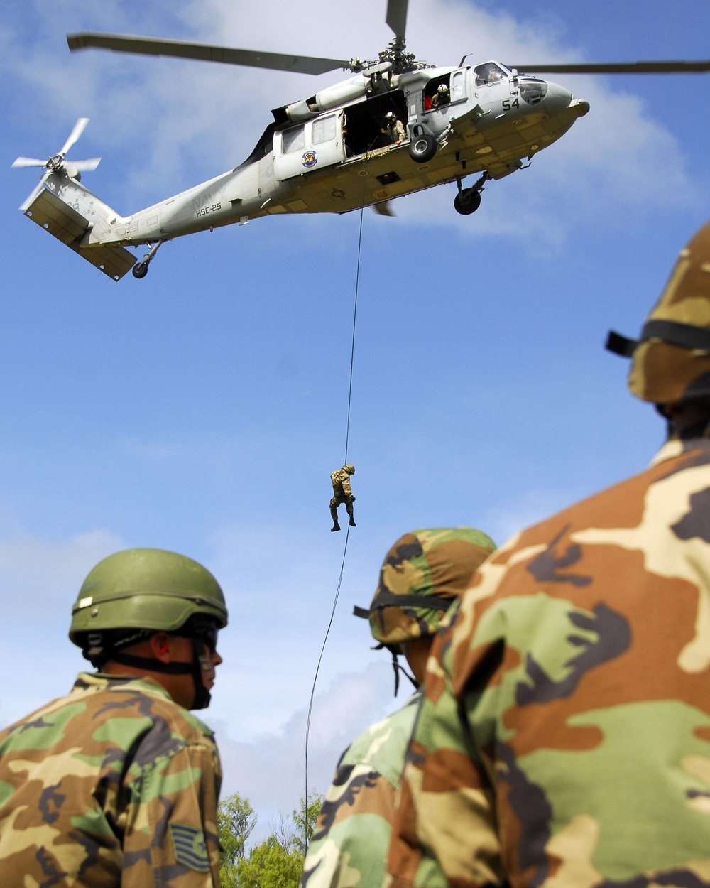 Airmen watch as a fellow team member repels from an HH-60 Pave Hawk helicopter.