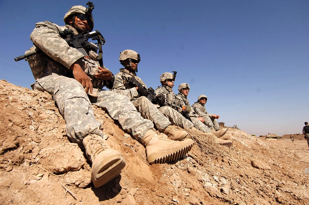 U.S. Army soldiers and Iraqi army soldiers sit on a dirt berm.