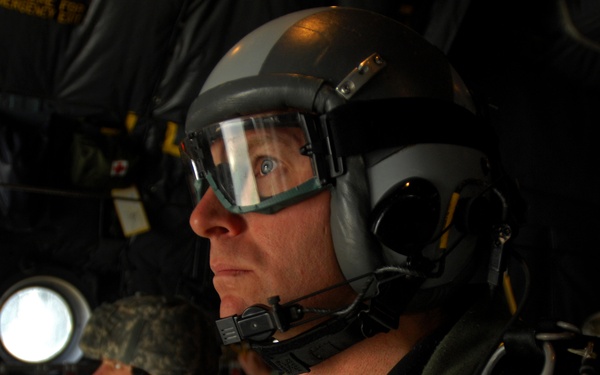 A U.S. Air Force pararescueman looks out the back of a C-130 Hercules aircraft.