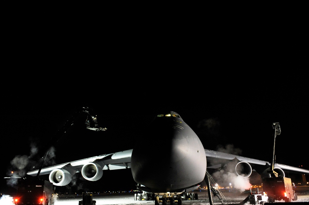 Two de-icing vehicles work on a C-5M Super Galaxy aircraft.