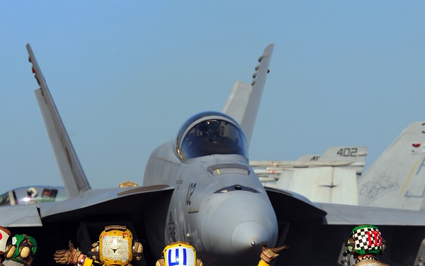 A U.S. Navy F/A-18E Super Hornet aircraft is directed toward a catapult.