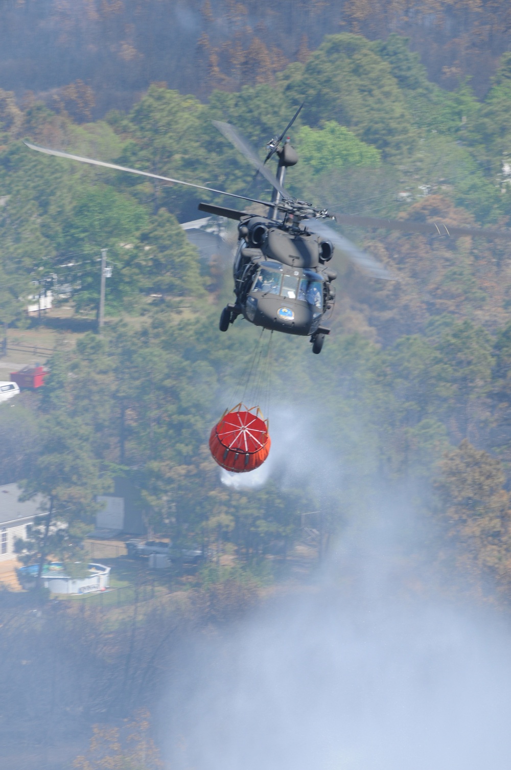A U.S. Army UH-60 Blackhawk helicopter drops 600 gallons of water onto fires.