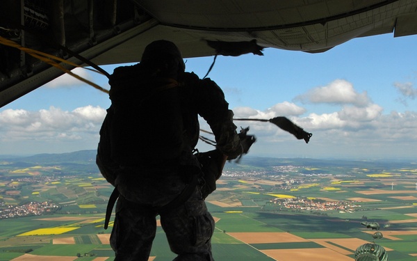 U.S. Air Force and Army paratroopers jump from the tail gate of a C-130J Super Hercules cargo aircraft.