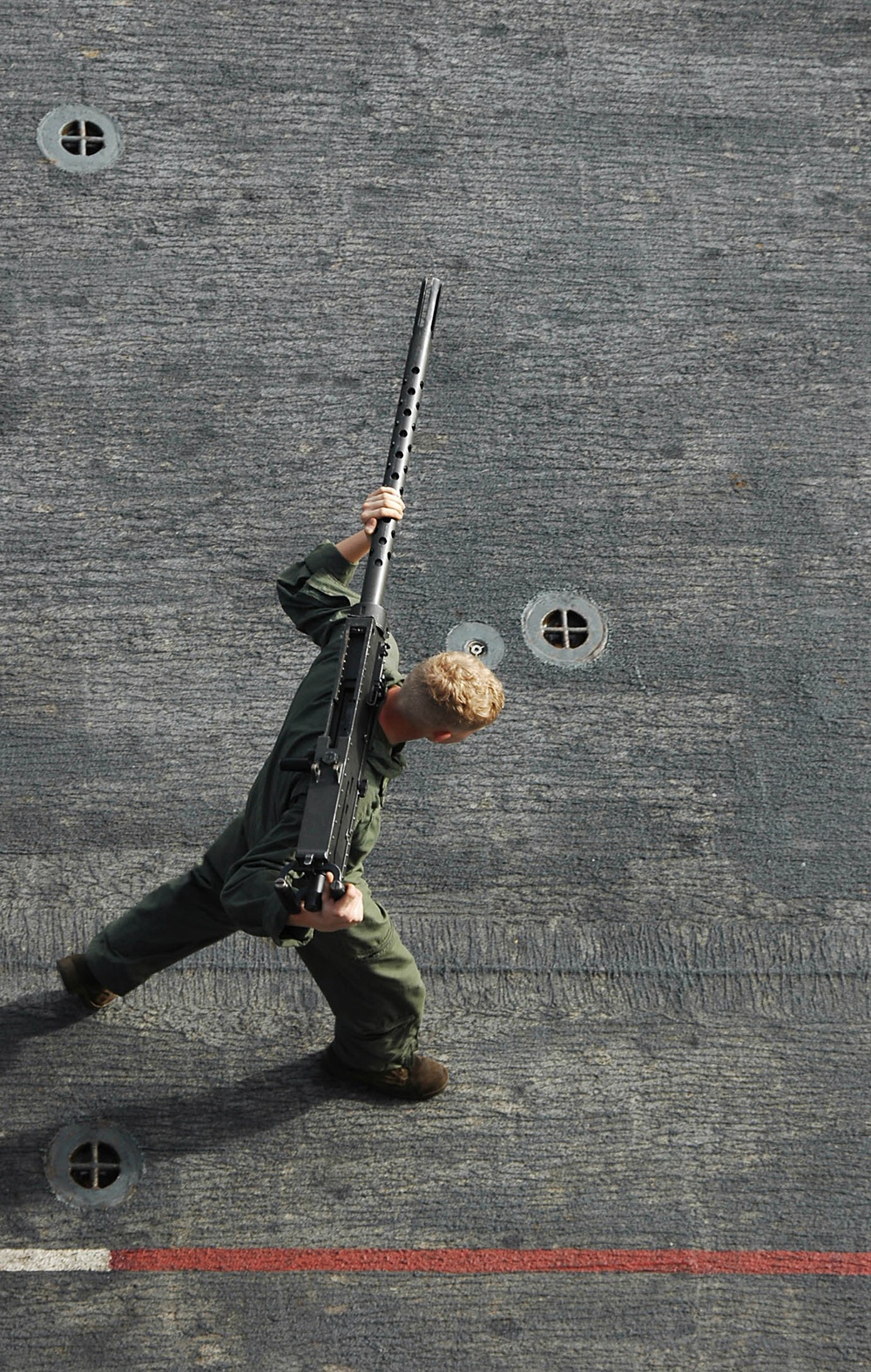 A U.S. Marine carries a .50 caliber machine gun across the flight deck.