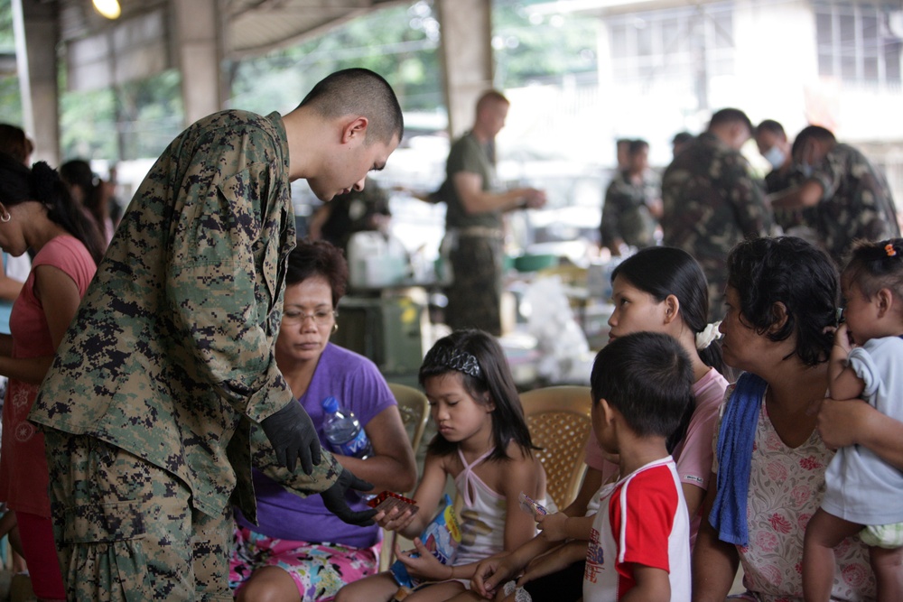 Petty Officer 2nd Class Raulito Galgana hands a patient medicine at an evacuation center in the Philippines.