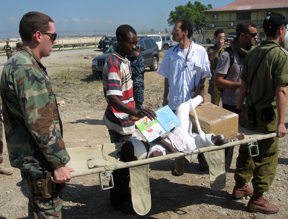 A U.S. Navy sailor and an Israeli soldier carry a Haitian girl to a waiting helicopter.