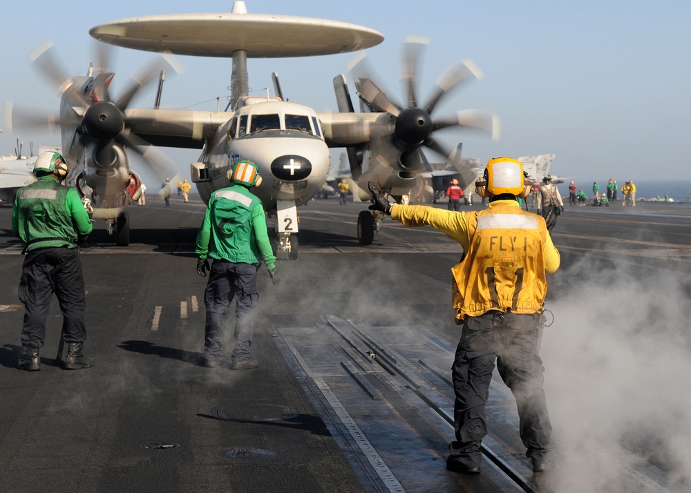A U.S. Navy sailor directs an E-2C Hawkeye aircraft up to the catapult.