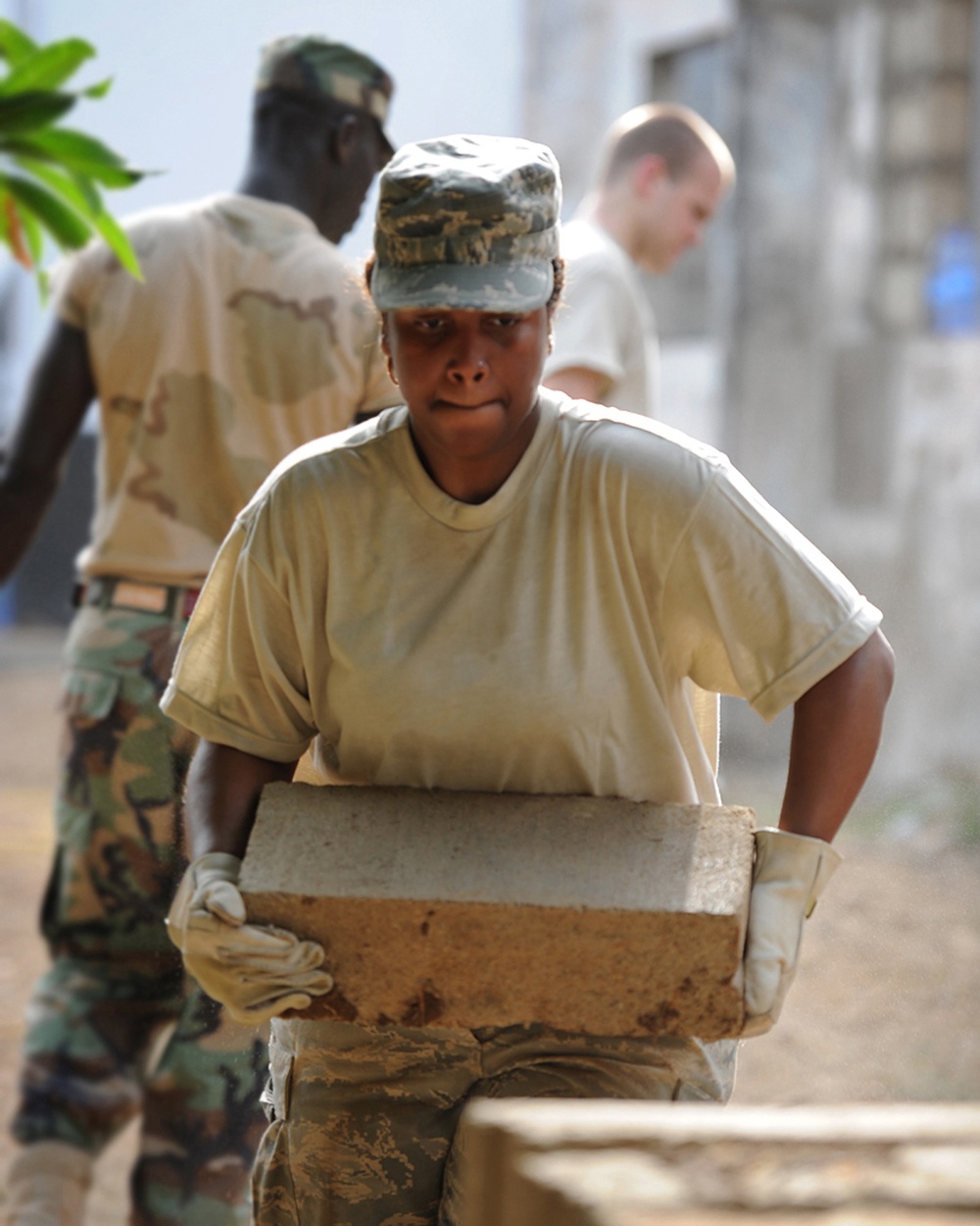 Senior Airman Shamika Moore carries a cement building block at a work site.