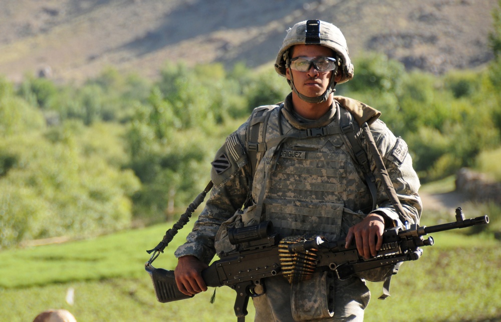 Spc. Brandon Rodriguez carries an M240 machine gun as he maneuvers through rough terrain.