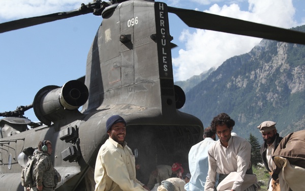 Pakistani men throw a bag of flour onto a pile behind a U.S. Army CH-47 Chinook helicopter.