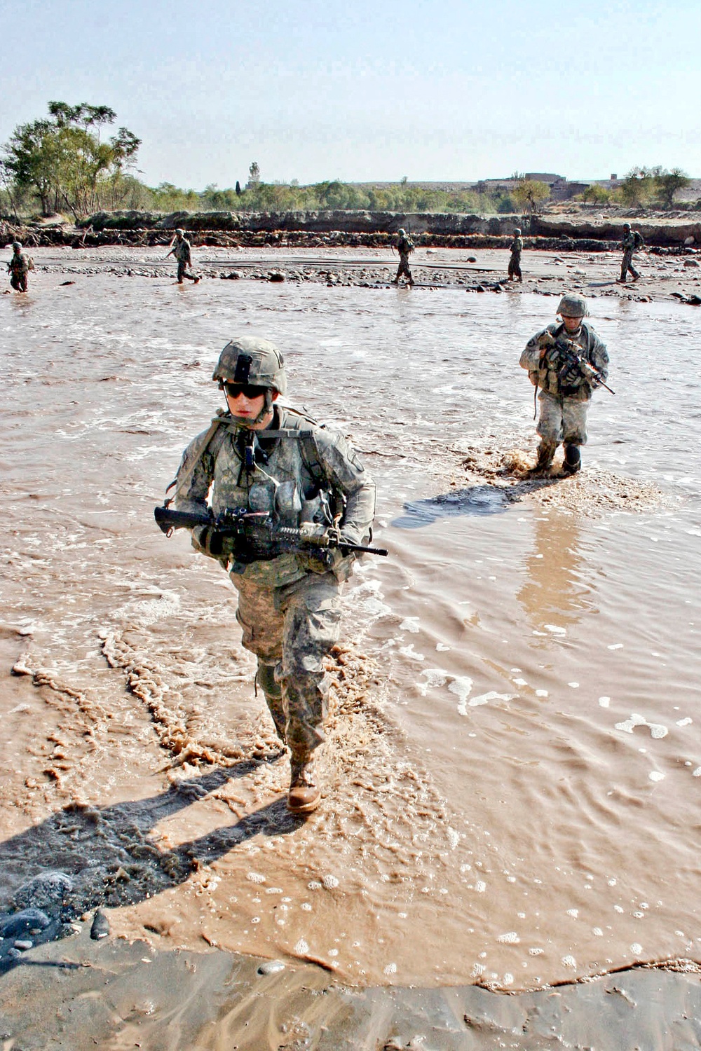 Spc. Jacob Phillips and Spc. Bjorn Goller Hagord cross a river of waist-high muddy water .
