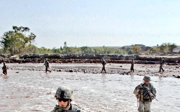 Spc. Jacob Phillips and Spc. Bjorn Goller Hagord cross a river of waist-high muddy water .